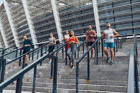 Group of young people in sports clothing jogging while exercising on the stairs outdoorsの写真素材