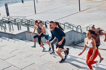 Top view of young people in sports clothing jogging while exercising on the stairs outdoors