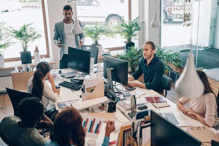 Group of young modern people in smart casual wear communicating and using modern technologies while working in the officeの写真素材