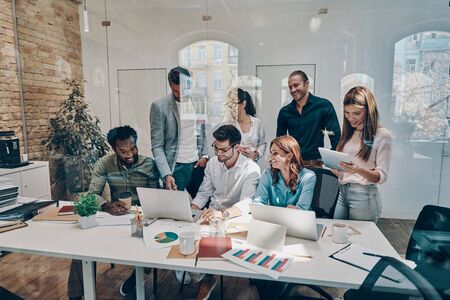 Group of young modern people in smart casual wear communicating and using modern technologies while working in the officeの写真素材