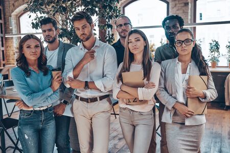 Group of young modern people in smart casual wear looking at camera while standing in the officeの写真素材