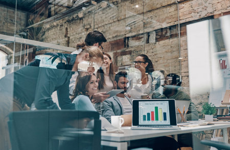 Group of young modern people in smart casual wear communicating and using modern technologies while...