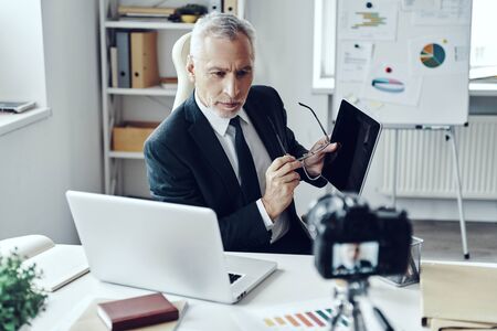 Senior man in elegant business suit using digital tablet while making social media videoの写真素材