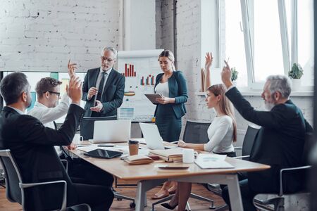 Successful business professionals voting with show of hands while working together in the modern officeの写真素材