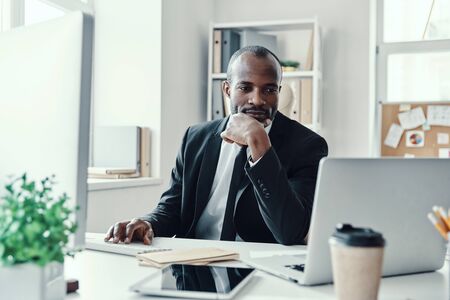 Concentrated young African man in formalwear using modern technologies while working in the officeの写真素材