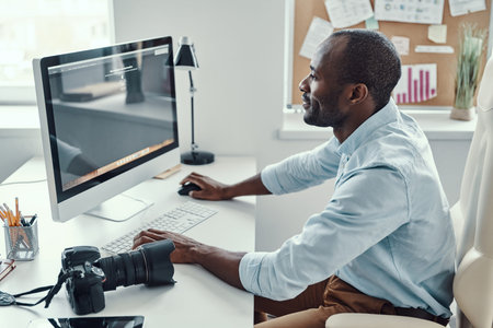 Handsome young African man using computer and smiling while working in the modern office