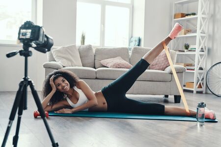 Happy young African woman exercising using strap and smiling while making social media videoの写真素材