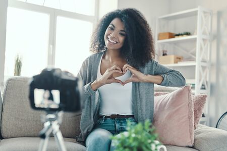 Cute young African woman showing heart with her hands and smiling while making social media videoの写真素材