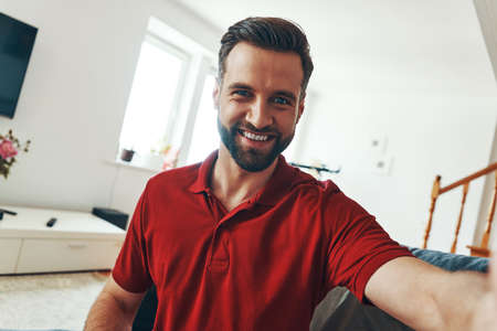 Handsome young man in casual clothing looking at camera and smiling while spending time indoorsの写真素材