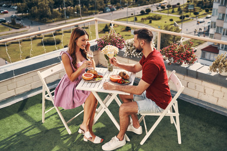 Top view of carefree young couple in casual clothing enjoying romantic dinner and smiling while sitting on the rooftop patio outdoorsの写真素材