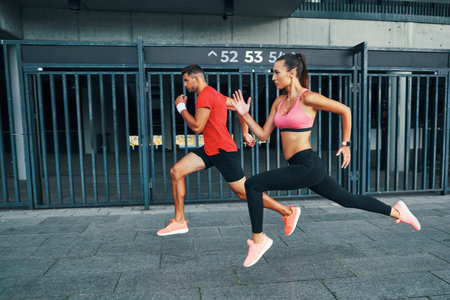 Full length of two athletes in sports clothing hovering in long jump while practicing outdoors