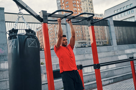 Handsome young man in sports clothing doing pull ups while exercising outdoors on the city street