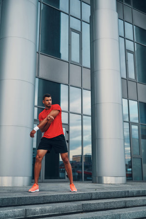Full length of handsome young man in sports clothing stretching while exercising outdoors