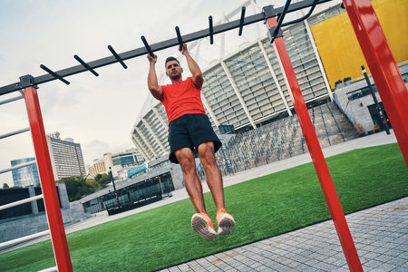 Full length of determined to win young man in sports clothing doing pull ups while exercising...