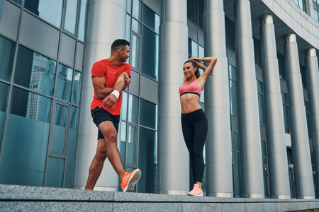 Full length of cute young couple in sports clothing warming up and smiling while practicing outdoors...