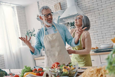 Cheerful senior couple preparing to cook a dinner and smiling while spending time at homeの写真素材