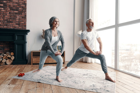 Good looking senior couple in sports clothing exercising and smiling while spending time at home