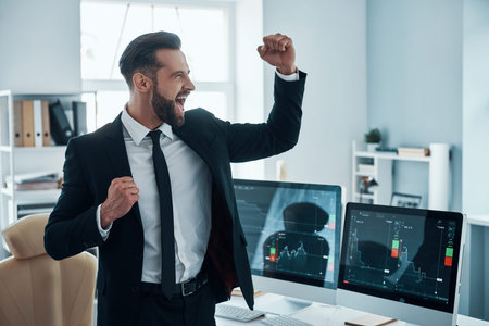Happy young man in shirt and tie cheering and gesturing while working in the office