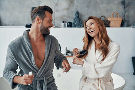 Couple in bathrobes smiling and cleaning teeth while doing morning routineの写真素材