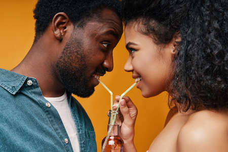 Beautiful young African couple drinking juice and smiling while standing face to faceの写真素材