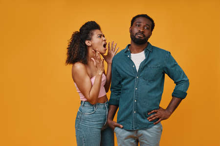 Irritated young African couple gesturing and having conflict while standing against yellow backgroundの写真素材