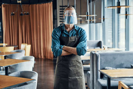 Confident male waiter in protective face shield keeping arms crossedの写真素材