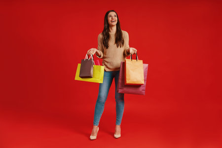 Full length of beautiful young woman in casual clothing carrying shopping bags and smiling