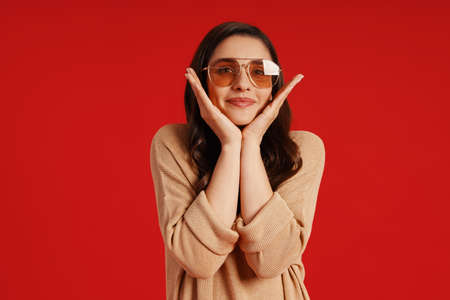 Beautiful young woman in casual clothing smiling while standing against red backgroundの写真素材