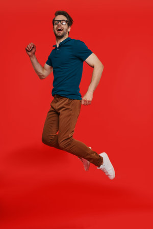 Full length of happy young man in casual wear jumping against red background
