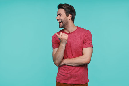 Handsome young man in casual clothing pointing away and smiling