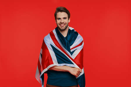Handsome young man in casual wear carrying British flag on shoulders and smilingの写真素材