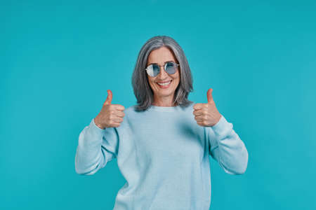 Mature beautiful woman looking at camera and keeping thumbs upの写真素材