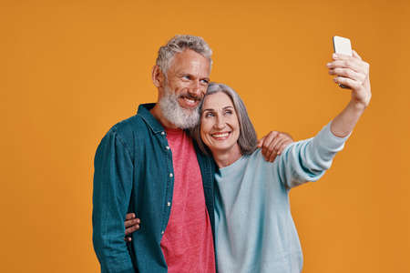 Happy senior couple smiling and using smart to take a selfieの写真素材