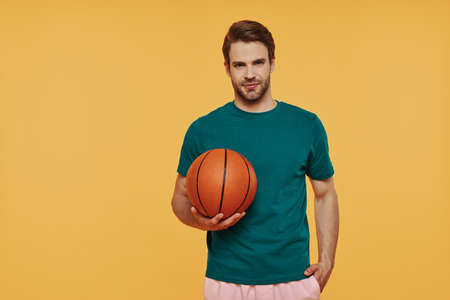 Handsome young man holding basketball ball and looking at cameraの写真素材