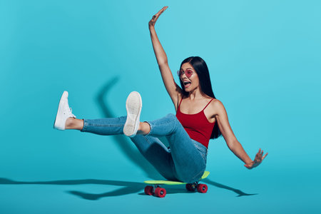 Playful young woman smiling while skateboarding against blue background