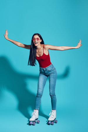 Full length of attractive young woman looking at camera and smiling while skating against blue...