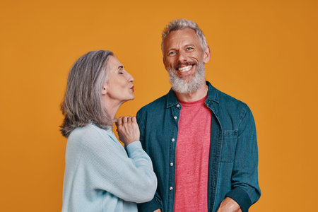 Beautiful senior couple smiling while standing together against orange background