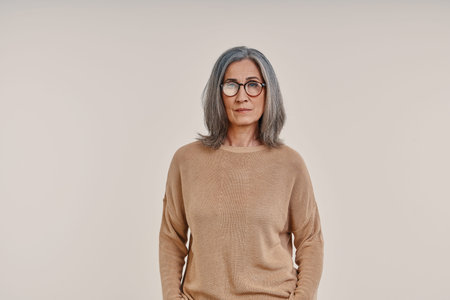 Mature beautiful woman looking at camera while standing against grey background