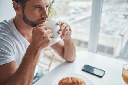 Top view of relaxed young man enjoying hot coffee while sitting at the kitchenの写真素材