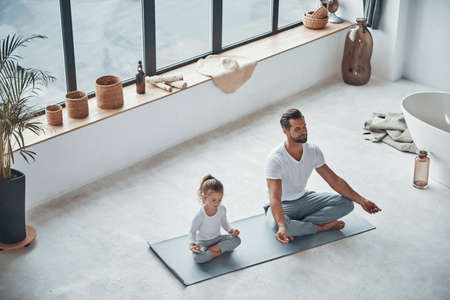 Top view of father and daughter doing yoga while sitting in lotus position at homeの写真素材