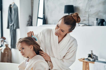 Beautiful young mother combining her daughter hair while doing morning routineの写真素材