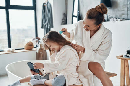 Beautiful young mother combining her daughter hair while doing morning routineの写真素材