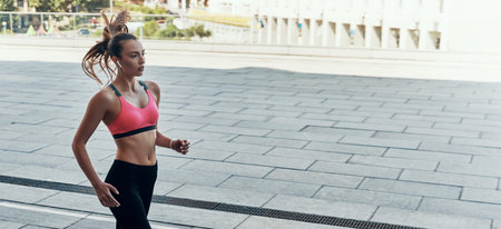 Beautiful young woman in sports clothing running outdoors