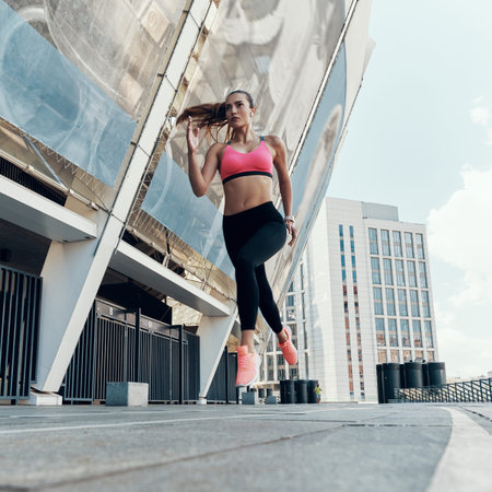 Full length low angle view of beautiful young woman in sports clothing running outdoors