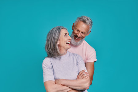 Happy senior couple bonding and smiling while standing together against blue background