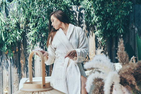 Beautiful young woman moisturizing hand cream while leaning at the bathtub outdoorsの写真素材