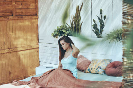 Beautiful young woman adjusting hair while waking up in the morningの写真素材