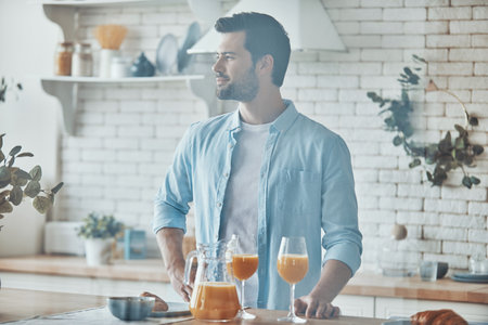 Handsome young man enjoying breakfast while spending time in the domestic kitchenの写真素材