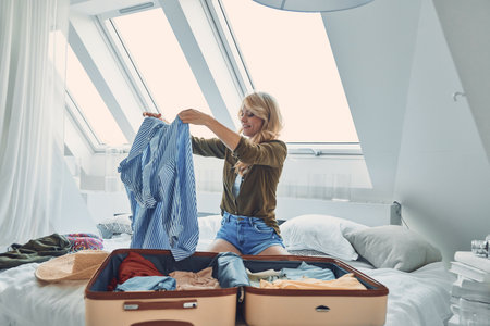 Attractive young woman packing luggage while sitting in bed at homeの写真素材