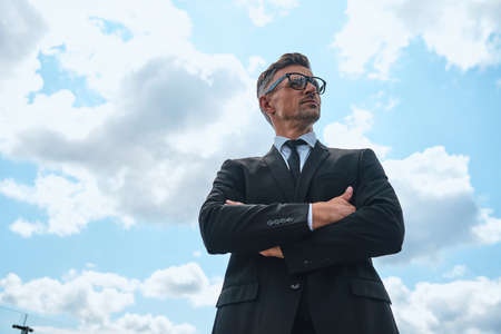 Low angle view of confident mature man in full suit keeping arms crossedの写真素材